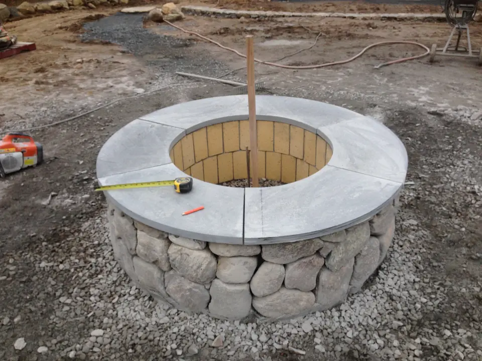A fire pit going up: fieldstone ring and bluestone cap on a crushed stone base