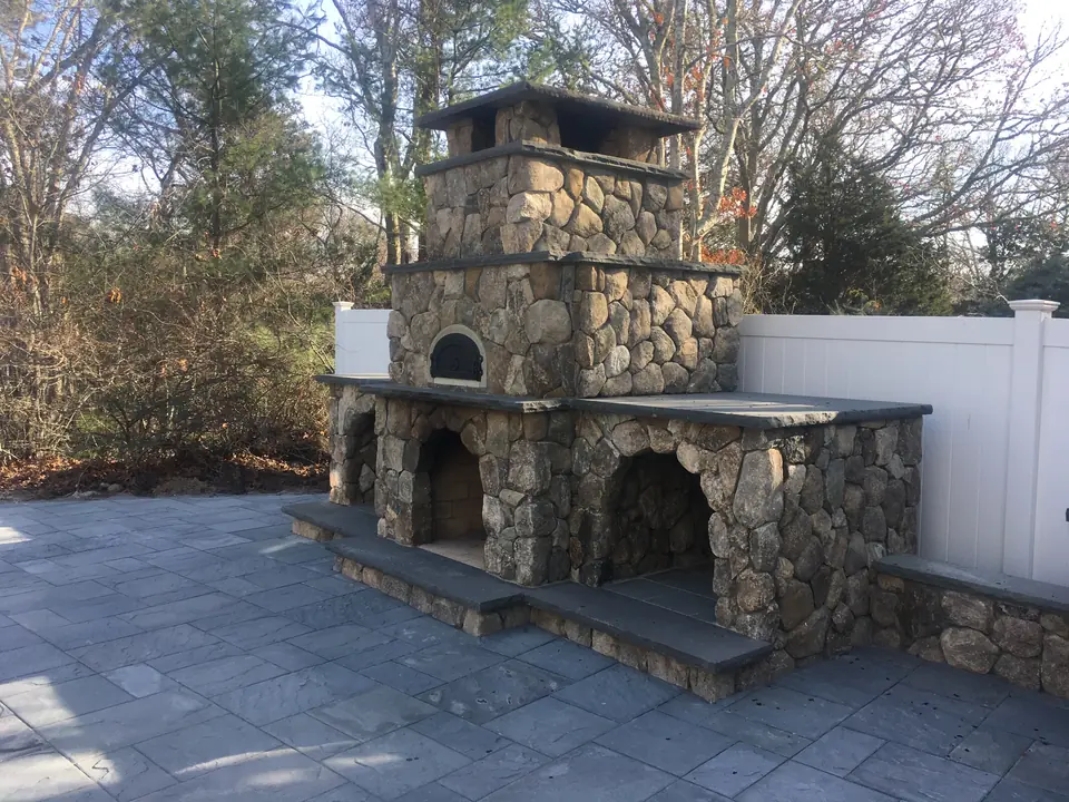 Fieldstone outdoor fireplace with arched wood boxes and a bluestone hearth